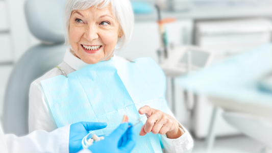 Smiling senior woman at the dentist's office holding dentures during a dental checkup, highlighting denture care and oral health.