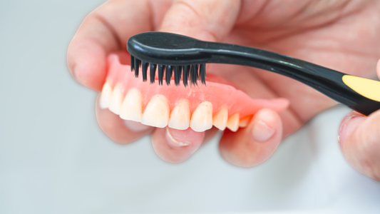 Person cleaning dentures with a black toothbrush as part of a daily denture care and maintenance routine.