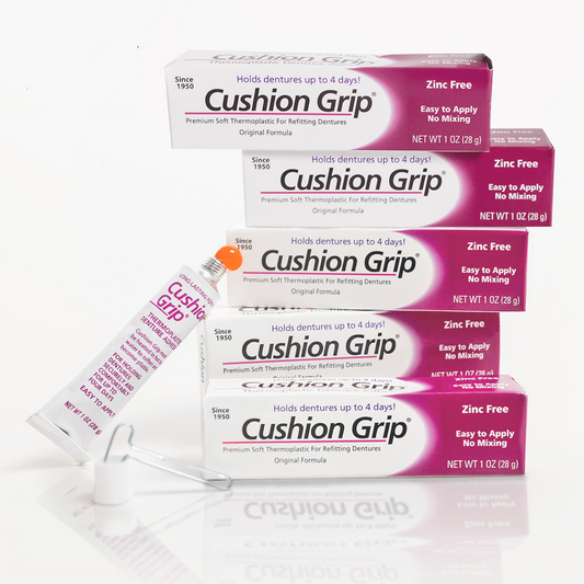 Multiple boxes and a tube of Cushion Grip denture adhesive on a white background